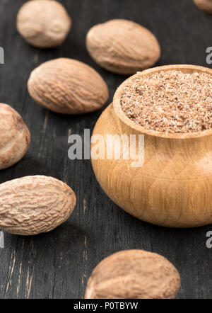 Pot avec de la muscade en poudre et parsemée de noix sur fond de bois Banque D'Images