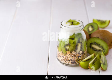 Yaourt blanc avec du muesli dans un bol en verre avec des morceaux de kiwi sur haut et morceaux entiers sur le côté droit. Banque D'Images