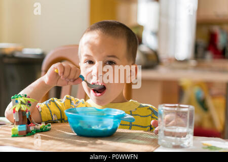 Le garçon 4 ans mange du porridge. Table enfant. Le concept de l'indépendance de l'enfant. Le garçon est déjeunant avec un appétit sur l'arrière cuisine Banque D'Images