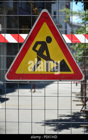 Le panneau d'avertissement 'en construction' est attaché à une clôture en treillis métallique avec un rouge et blanc rayé de bandes de signal Banque D'Images