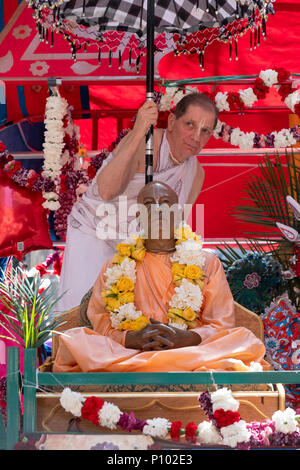 Un homme dans un sari blanc tenant un parasol au-dessus d'une statue du fondateur du mouvement Hare Krishna à l'Rathayatra festival à Midtown Manhattan. Banque D'Images