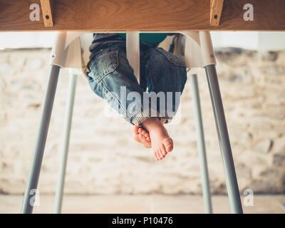 Les jambes d'un petit enfant assis sur une chaise haute à la table à manger Banque D'Images