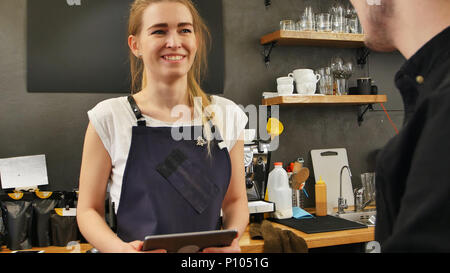 Portrait d'une femme magnifique en tenant la barista, commande d'un client avec un ordinateur Tablet and smiling Banque D'Images