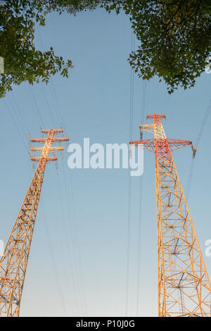 Deux grands haute tension rectangulaire tours de transmission électriques avec les lignes électriques et les arbres au-dessus des isolateurs sous ciel partiellement nuageux Banque D'Images