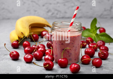 Les smoothies banane cerise dans un bocal en verre, de cerises fraîches et des bananes sur un fond de béton gris Banque D'Images