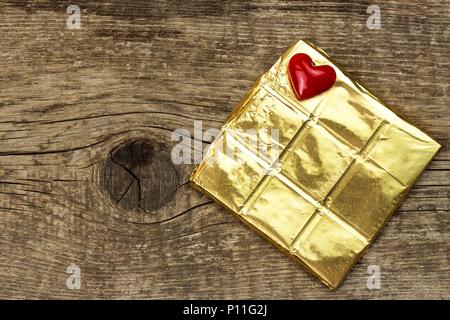 Chocolat amer dans une feuille d'or sur une planche de bois. La délicatesse du chocolat Banque D'Images