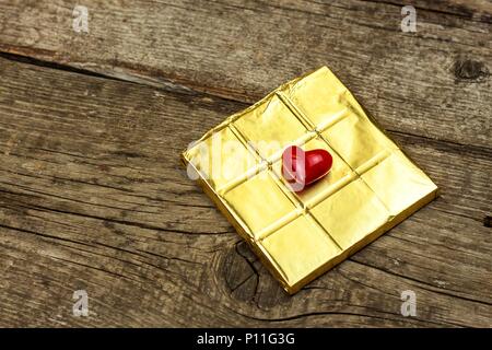 Chocolat amer dans une feuille d'or sur une planche de bois. La délicatesse du chocolat Banque D'Images