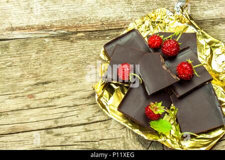 Chocolat amer dans une feuille d'or sur une planche de bois. La délicatesse du chocolat. Les Fraises sauvages Banque D'Images