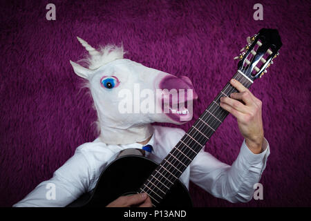 Freaky jeune homme en masque comique à jouer de la guitare sur le fond violet. Portrait de guy inhabituelle en chemise et cravate avec instrument de musique Banque D'Images