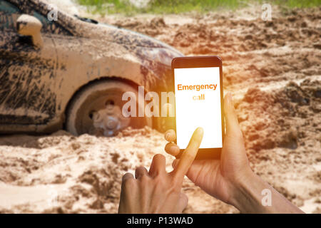 L'homme la main à l'aide d'urgence à l'aide d'appel smartphone pneu de voiture coincé dans la boue arrière-plan. Roue de voiture dans la boue, l'argile peut ne pas manquer. Banque D'Images