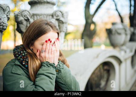 Jeune femme séduisante avec des clous rouges couvrant son visage avec les mains Banque D'Images