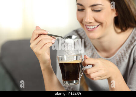 Close up of a happy girl throwing du sucre dans le café avec une cuillère, assis sur un canapé dans la salle de séjour à la maison Banque D'Images