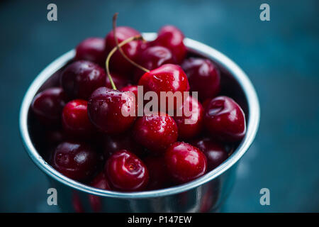 Cerises avec un petit seau en métal sur une base de béton gris, l'été des petits fruits concept avec copie espace. Des tons de couleur neutre still life Banque D'Images