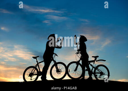 Couple de cyclistes frappant des mains ensemble. Cheerful couple avec vélo s'amusant sur fond de ciel en soirée. Date romantique sur hill au coucher du soleil. Banque D'Images