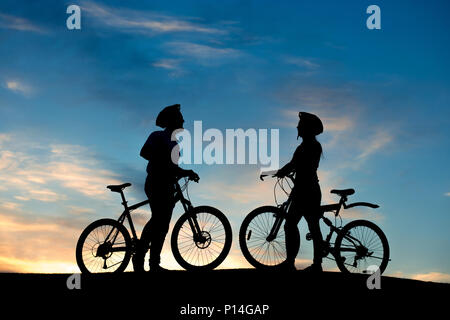 Silhouettes de jeunes amoureux au coucher du soleil. Couple aimant de cyclistes bénéficiant de l'autre tout en se tenant sur la colline parlementaire le fond de ciel en soirée. Banque D'Images