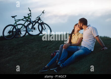 Couple romantique baiser est à l'extérieur. Jeune homme et femme dans l'amour est un baiser au cours de promenade en vélo sur la colline verte. L'amour et la romance concept. Banque D'Images