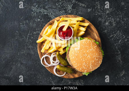 Burger, hamburger ou cheeseburger accompagné de frites, les cornichons et l'oignon sur planche de bois. Vue d'en haut. Concept de restauration rapide Banque D'Images