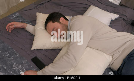 Jeune homme fatigué se trouve sur le lit et s'endort après une dure journée de travail Banque D'Images