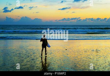 Aller surfer à surfer dans l'océan au coucher du soleil. L'île de Bali, Indonésie Banque D'Images