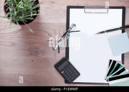 Vue de dessus.Presse-papiers avec une feuille blanche, un stylo, lunettes et calculatrice sur fond de bois Banque D'Images