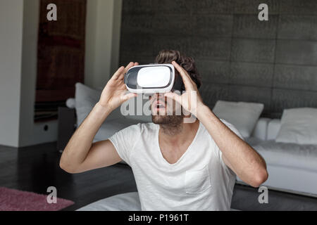 Jeune homme barbu avec des lunettes VR étonné par le cyberespace à la maison Banque D'Images