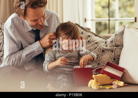 Père et fille assise sur un canapé de l'ouverture d'une boîte-cadeau. Petite fille explore la boîte cadeau pendant que son père regarde sur. Banque D'Images