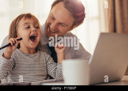 Fille jouant avec un stylo et de rire alors qu'il était assis avec son père au travail avec ordinateur portable et tasse de café sur la table. Père de passer du temps avec d Banque D'Images