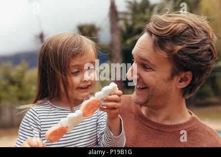 Fille heureuse avec son père tenant un bâton de sucre candy à l'extérieur. Père et fille de passer du temps ensemble manger du sucre candy. Banque D'Images