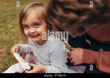 Smiling girl sitting avec son père à l'extérieur tenant un bâton de sucre candy. Père et fille de passer du temps ensemble manger du sucre candy. Banque D'Images