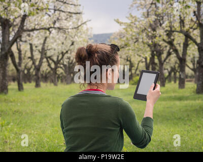 Vue arrière d'une jeune femme à l'extérieur la lecture sur son ebook Banque D'Images