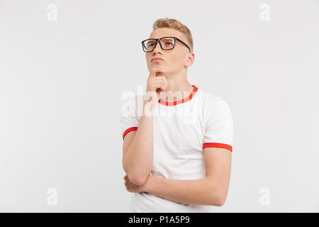 Image of male student wearing eyeglasses à vers le haut tout en reflétant et toucher le menton plus isolé sur fond blanc Banque D'Images