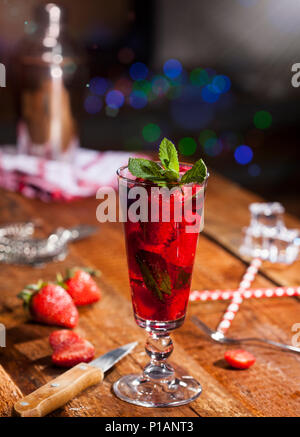 Boisson froide d'été avec des fraises, de la menthe et de la glace en verre sur le comptoir du bar en bois. Gros plan du cocktail avec de petits fruits rouges frais. Banque D'Images