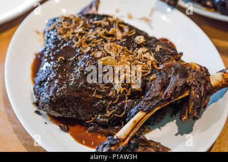 Épaule d'agneau fumé croustillant avec les oignons et la sauce à l'agneau, sur un plateau blanc. Banque D'Images