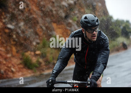 Jeune homme dédié à vélo sur route pluvieuse Banque D'Images