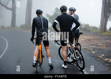 Amis cyclistes masculins en faisant une pause, reposant sur route mouillée Banque D'Images