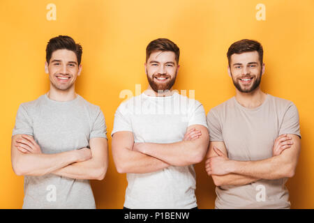 Trois jeunes hommes souriant debout avec les bras croisés sur fond jaune isolé Banque D'Images