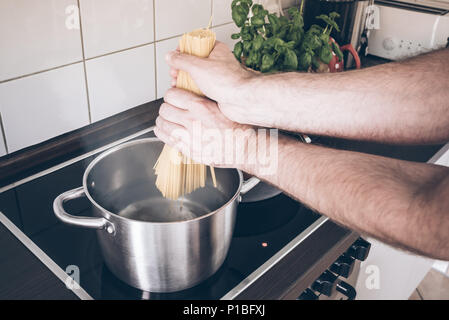 Mettre les mains dans le pot de spaghettis à l'eau bouillante sur la cuisinière Banque D'Images