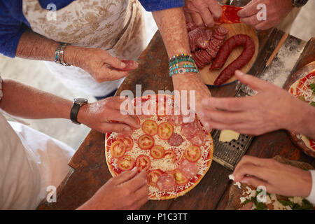 Vue aérienne senior friends ajouter les tomates et la viande pour pizzas fraîches Banque D'Images