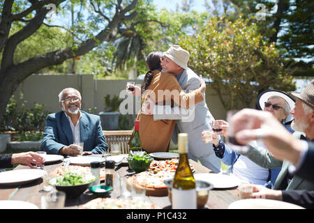 Friends toasting romantic couple hugging at sunny garden party Banque D'Images