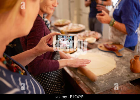 Femme avec téléphone appareil photo photographier ami faire la pâte à pizza en cours de cuisine Banque D'Images