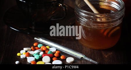 Médicaments et pilules sur une table en bois. Divers moyens pour prévenir les rhumes. Thé au citron et de miel. Tasse en verre avec plateau tranche de citron et un pot de miel. Banque D'Images