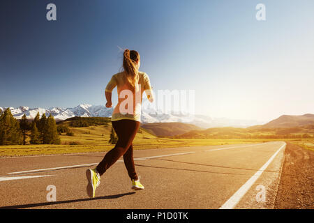 Femme s'exécute par route droite au coucher du soleil contre les montagnes. L'exécution en plein air concept Banque D'Images