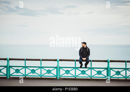 Tourist est assis sur une balustrade au bord de mer, la plage de Brighton, Brighton, Angleterre Banque D'Images