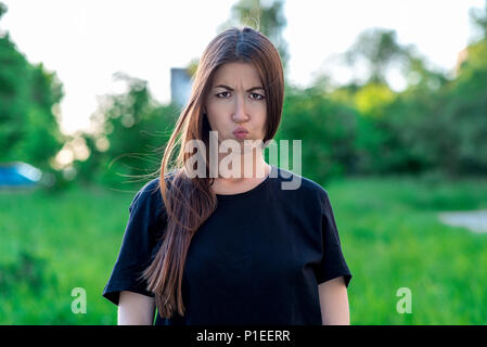 Fille en été dans le parc à l'air frais. Close-up portrait. La jeune fille fit la moue. Elle tira sur ses joues. Insatisfait d'expression. Brune avec des taches de rousseur. Kiss émotionnelle. Femme lunatique. Banque D'Images