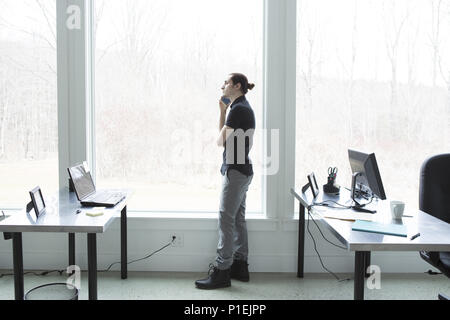 Un jeune homme d'affaires avec un petit pain parlant sur un téléphone portable dans un bureau moderne. Concept de brainstorming d'entreprise Banque D'Images