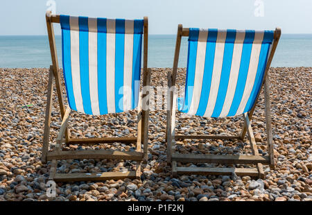 Deux ou rayé bleu et blanc à l'ancienne stripey transats en bois vide sur les galets et de galets de la plage à Brighton dans l'East Sussex ensoleillé. Banque D'Images