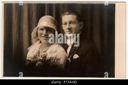 LIBEREC (REICHENBERG), RÉPUBLIQUE TCHÉCOSLOVAQUE - VERS 1920s : photo d'époque des jeunes mariés. La mariée porte un chapeau blanc avec dentelle (bobbin). Le marié porte des vêtements chic, un noeud papillon blanc. Ancienne photo en noir et blanc. Portrait de studio antique. 1920s Banque D'Images