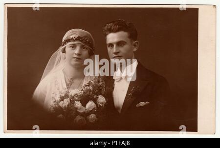 LIBEREC (REICHENBERG), RÉPUBLIQUE TCHÉCOSLOVAQUE - VERS 1920s : photo d'époque des jeunes mariés avec bouquet de mariage. La mariée porte l'adresse du voile de mariage. Le marié porte des vêtements chic, un noeud papillon blanc. Vieux portrait de studio noir et blanc. 1920s. Banque D'Images