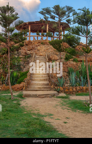 Escalier en pierre naturelle avec des buissons verts de part et d'autre menant à pergola en bois avec partiellement nuageux ciel en parc public à l'heure d'été Banque D'Images