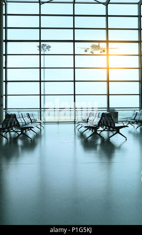Salon d'embarquement spacieux de l'aéroport avec de grandes baies vitrées du sol au plafond et des sièges passagers vides Banque D'Images